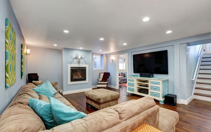 Finished Basement Living Area with Recessed Lighting Comfortable finished basement family room featuring blue walls, hardwood floors, a beige sectional sofa, fireplace, large television, and bright recessed ceiling lights.