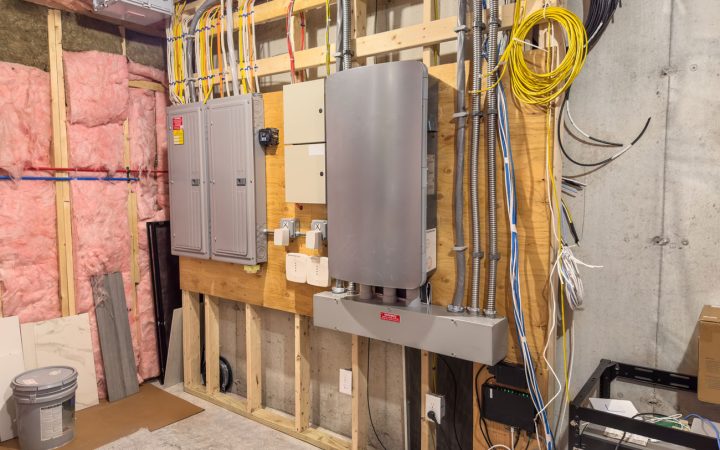 Unfinished Basement Electrical System Rough-In An extensive residential electrical setup in an unfinished basement featuring multiple breaker panels, a large inverter or battery backup system, and organized conduit wiring against exposed studs and insulation.