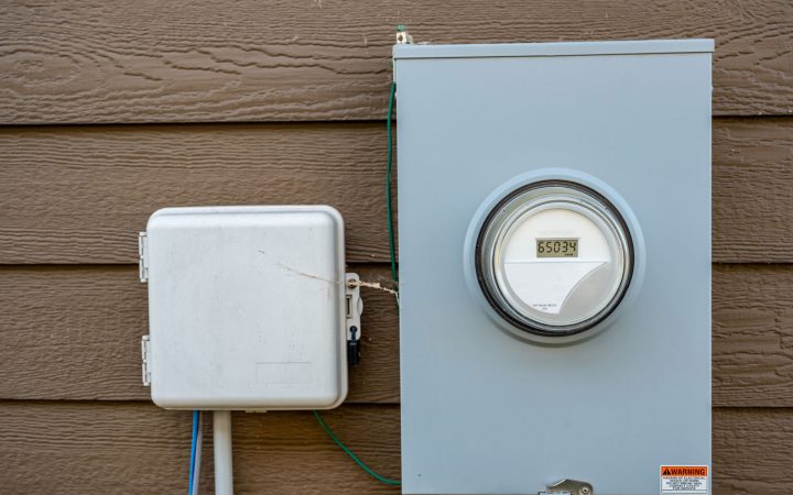 Exterior Digital Electric Meter Installation A modern digital electric meter and an adjacent utility box mounted on the brown siding of a house exterior.