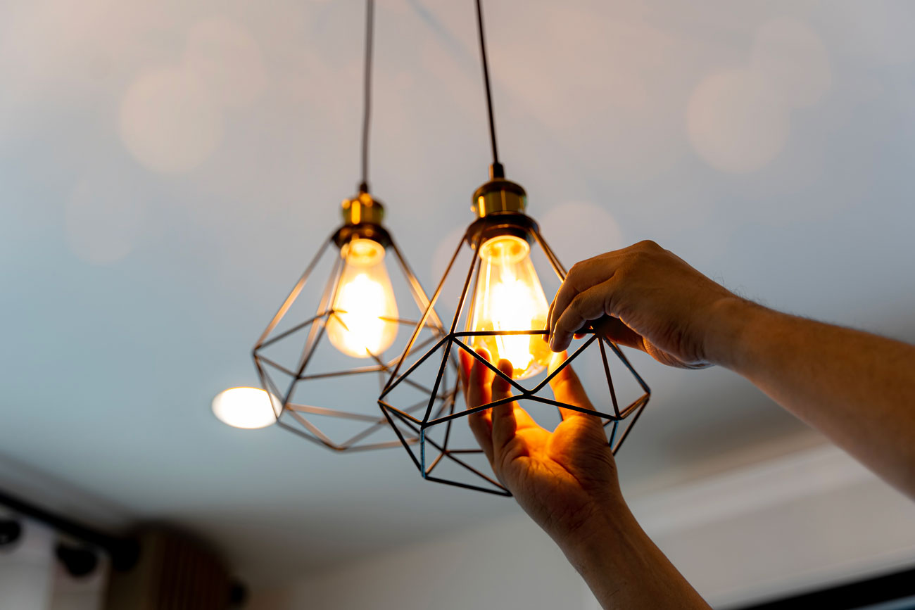 Modern Geometric Pendant Light Fixture Installation Close-up of hands installing or adjusting contemporary black wire geometric cage pendant lights with warm glowing Edison bulbs.