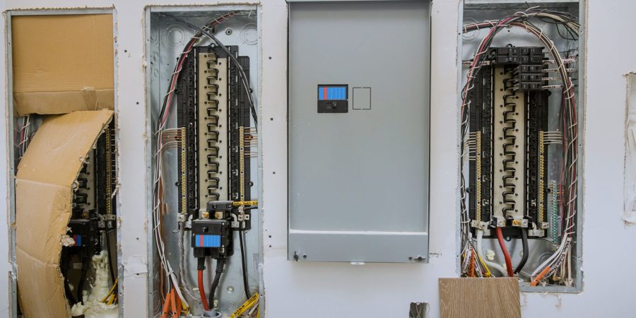 Residential Electrical Service Panel Upgrade and Wiring Wall-mounted electrical breaker panels during installation, showing exposed wiring and circuit breakers in open boxes alongside a closed gray metal panel cover.
