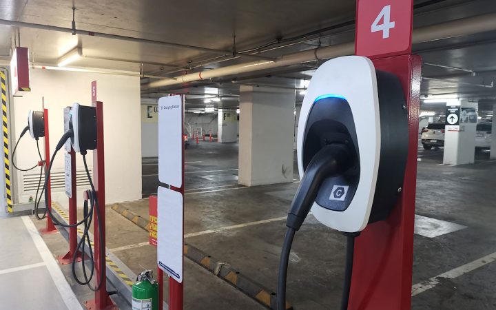 Commercial Parking Garage EV Charging Stations Multiple red and white electric vehicle charging stations installed in numbered parking spots within a well-lit indoor parking garage.