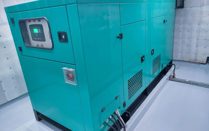Commercial Industrial Generator System Large teal-colored commercial backup generator installed in a mechanical room, featuring a digital control panel display, ventilation grilles, and professional indoor installation with gray flooring