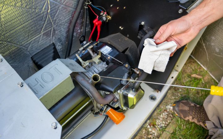 Generator Maintenance and Engine Inspection Technician performing routine maintenance on a generator engine, checking oil levels with a dipstick while holding a cleaning cloth, with exposed engine components and wiring visible