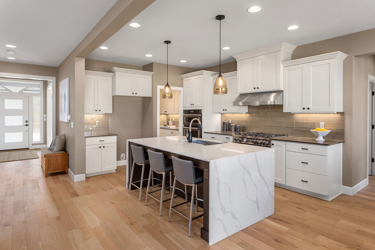 Modern Kitchen with Custom Pendant and Recessed Lighting A bright, modern kitchen featuring white cabinetry, a large island with a waterfall quartz countertop, and layered lighting including glass pendant lights over the island and recessed ceiling lights.