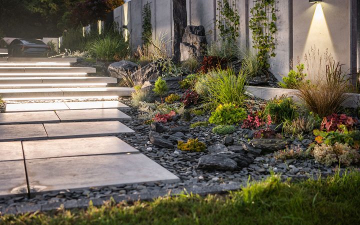 Modern Landscape Lighting and Stone Hardscaping Contemporary outdoor space featuring illuminated floating stone steps, a rock garden with varied vegetation, and wall sconces lighting up a concrete retaining wall.