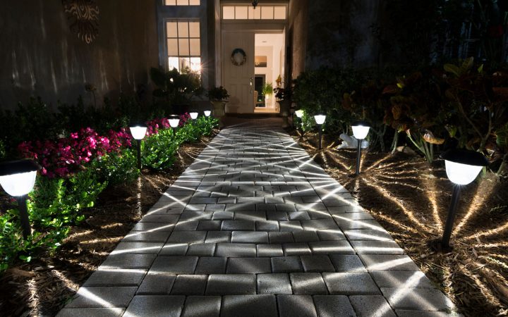Residential Pathway Lighting at Night A paved walkway leading to a front door illuminated by path lights that cast dramatic starburst shadows across the bricks and surrounding mulch beds.